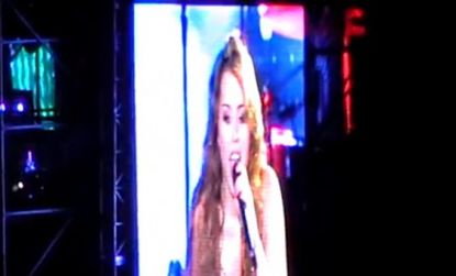Miley Cyrus, projected on a giant screen during her South American tour, belts out Nirvana's 1991 hit "Smells Like Teen Spirit" to her screaming tween fans. 