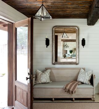 door open with pale wood bench and striped throw mirror and dark wood ceiling