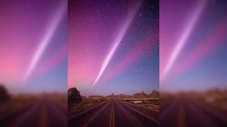 A streak of purple light hangs in the night sky above a desert