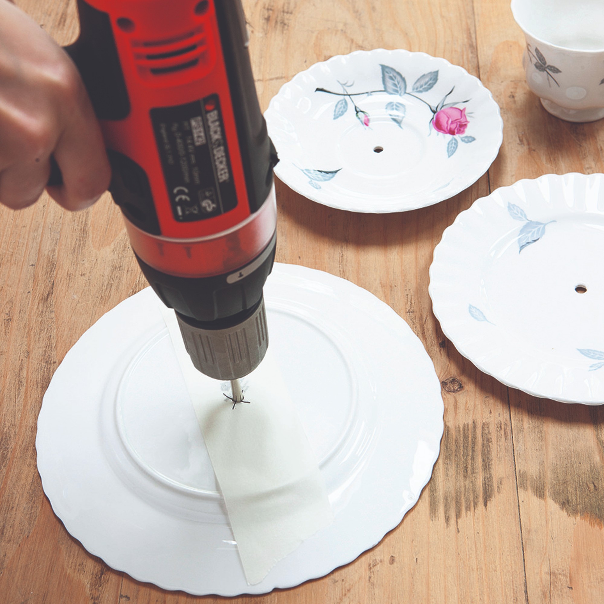 A set of plates being drilled with a red drill to hang on the wall