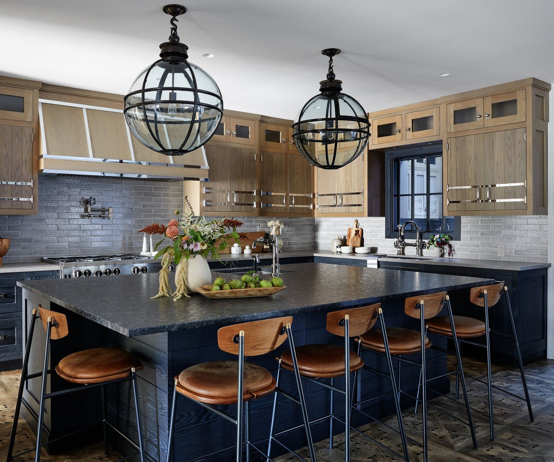 A kitchen with wooden cabinets and metallic details, and black kitchen island and black countertops
