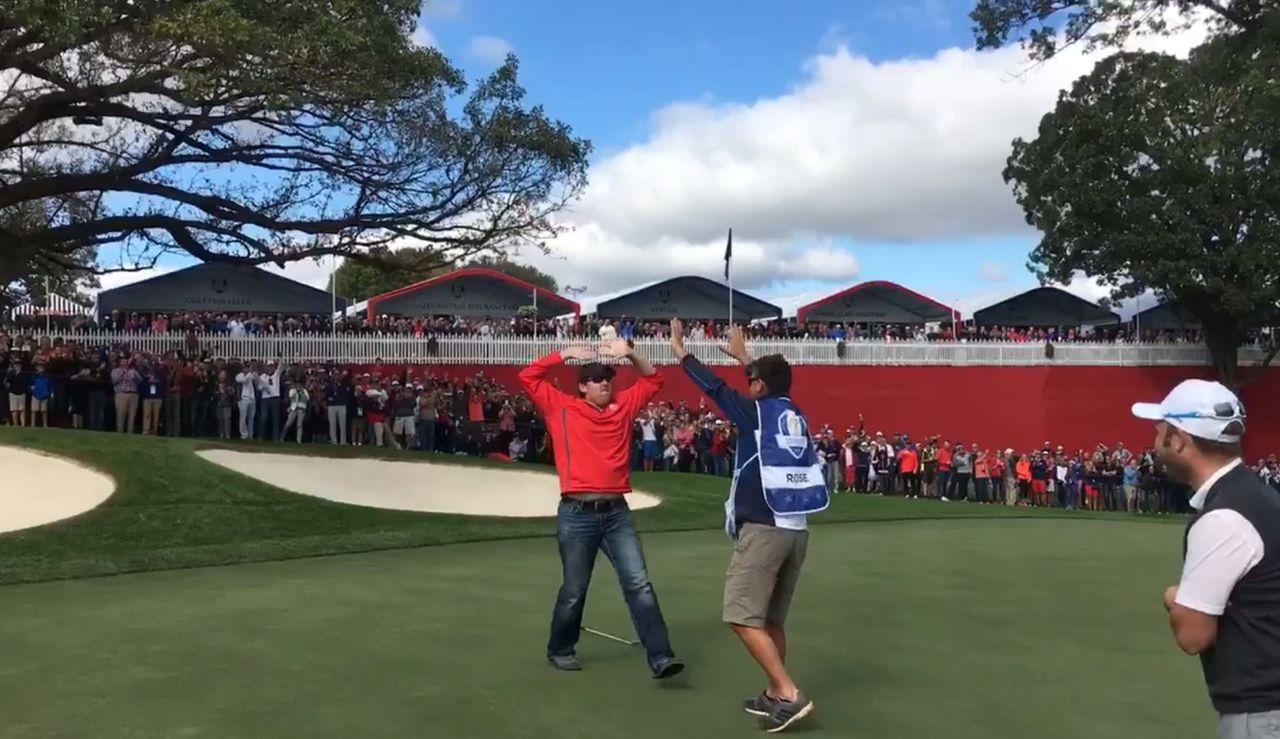 A man high fives a caddie after holing a putt