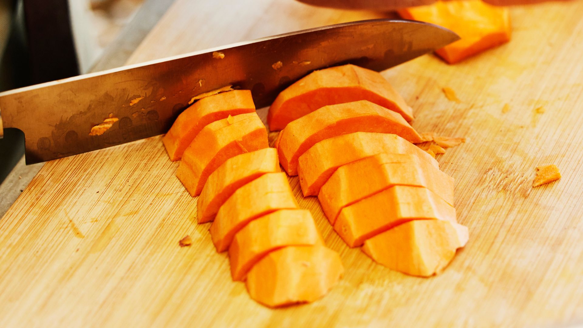 Sweet potato chopped with stainless steel knife on wooden chopping board