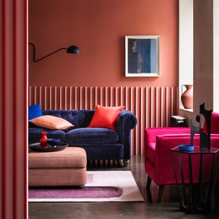 living room colour mistakes, living room with coral walls, blue sofa, bright pink armchair, houndstooth footstool, artwork, bright accessories