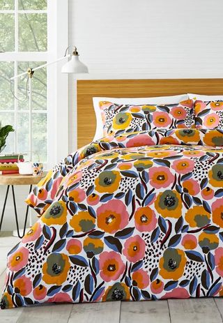 A floral, colorful bedding set with a wooden headboard and nightstand