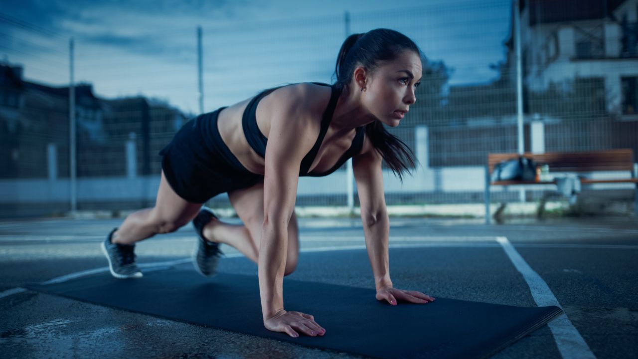 Beautiful Energetic Fitness Girl Doing Mountain Climber Exercises. She is Doing a Workout in a Fenced Outdoor Basketball Court. Evening Shot After Rain in a Residential Neighborhood Area.