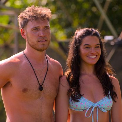 a shirtless jimmy p stands neck to a smiling ally in a bikini in a still from perfect match season 4