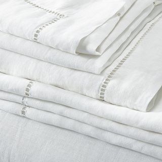 A pile of folded white linen bedding with a cut out detail trim along the edges