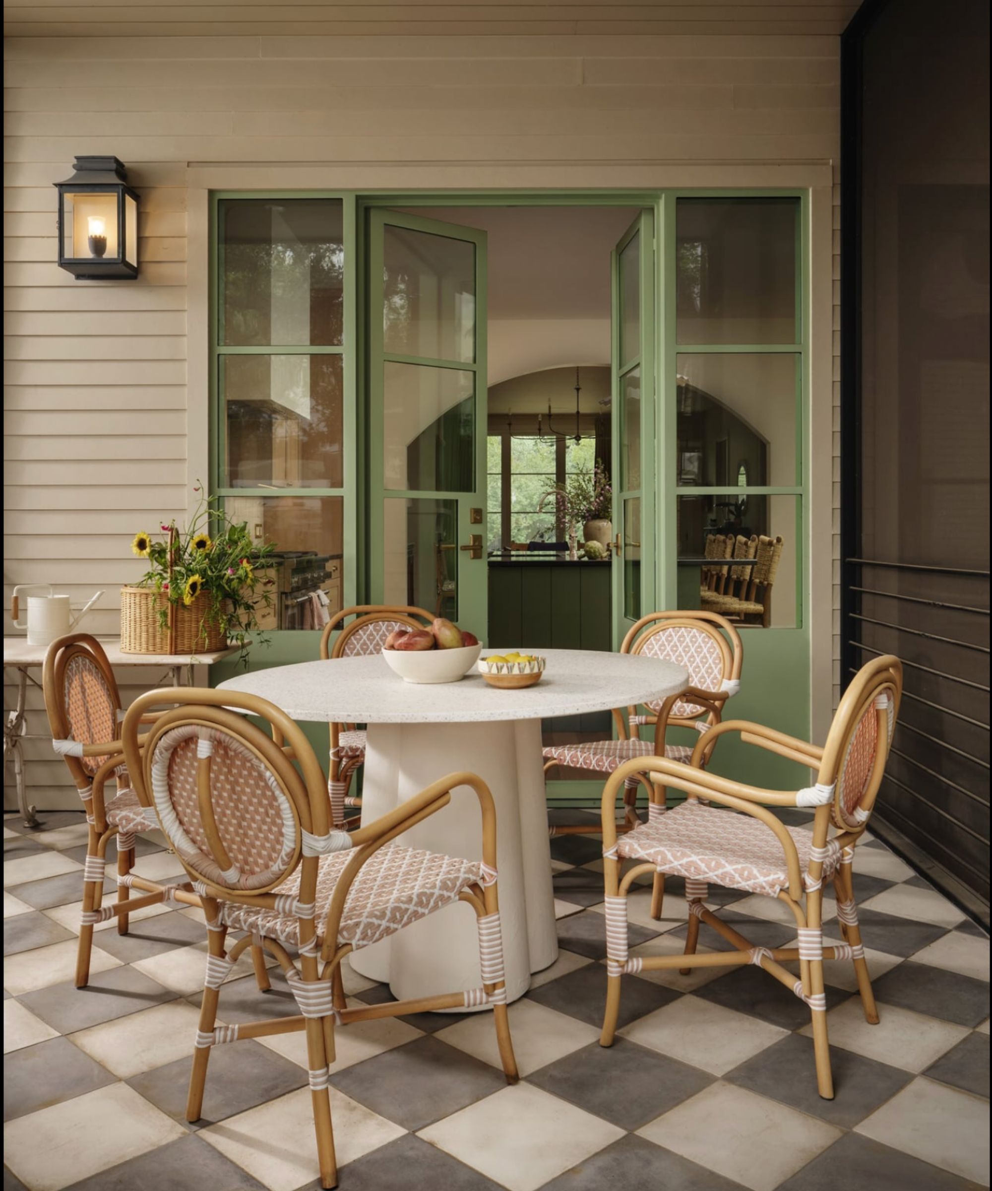 Patio with tiled floor, round white table, bistro chairs, green painted Crittall doors looking into kitchen