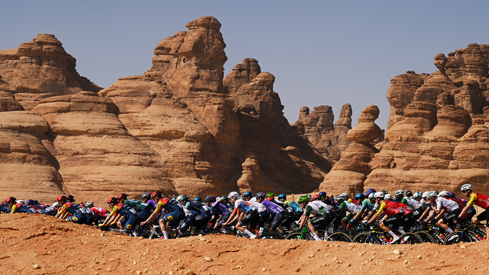 The peloton passes through a rocky landscape during Stage 2 of the 2026 AlUla Tour, near AlManshiyah, Saudi Arabia