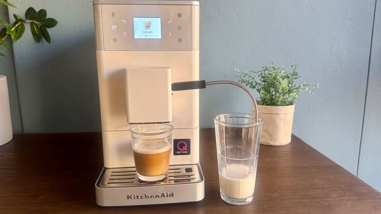KitchenAid KF3 coffee machine with a coffee on the drip tray and a glass of milk to the right.