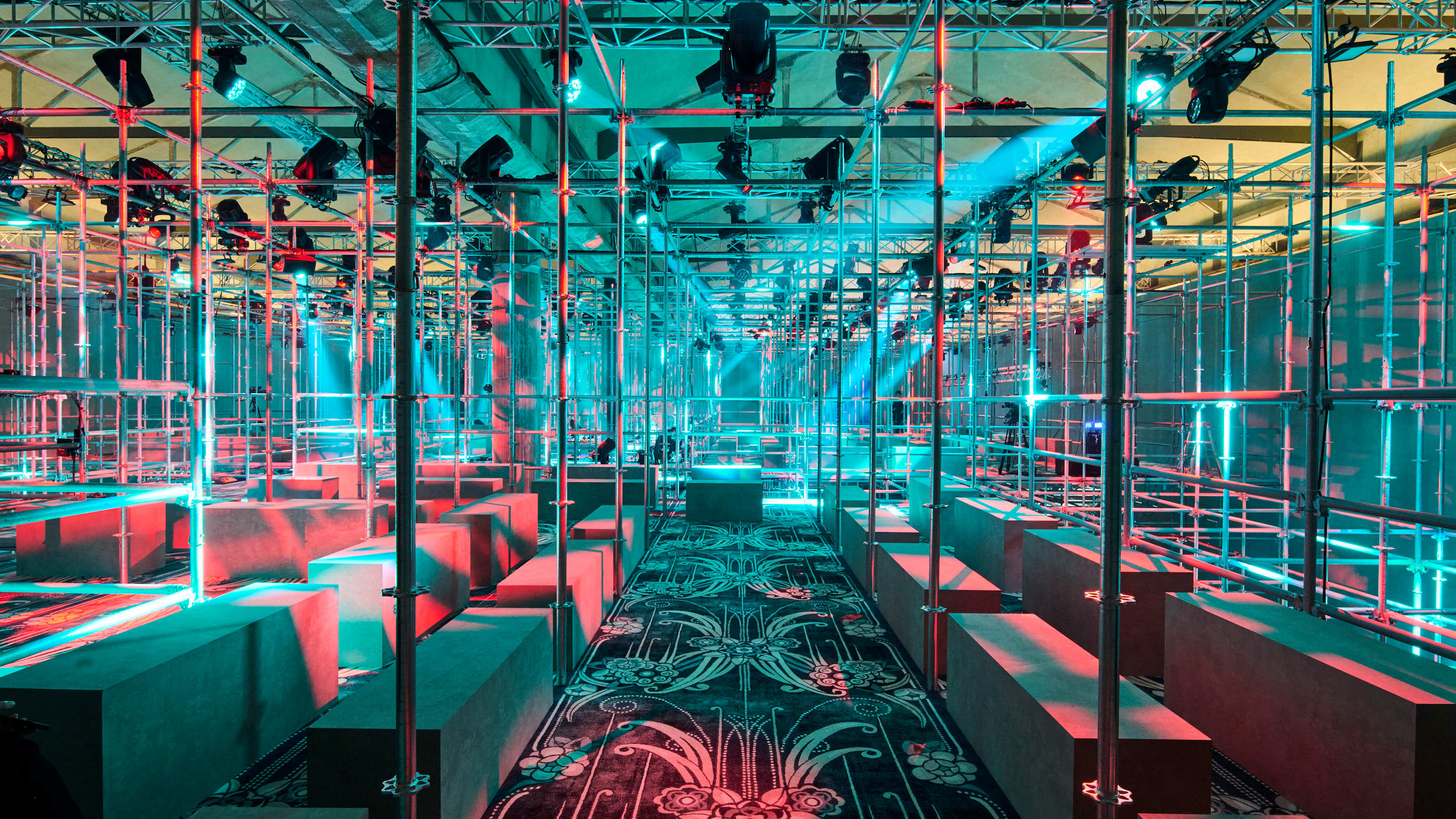 Prada A/W 2025 menswear runway show set featuring scaffolding and patterned carpet