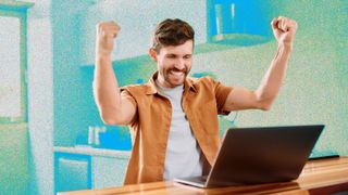 A young man looking excited while sitting at a table using a laptop.
