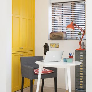 white wall with yellow door white round table grey chair red lamp