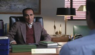 Iqbal Theba sitting at a desk talking to a student in Glee.