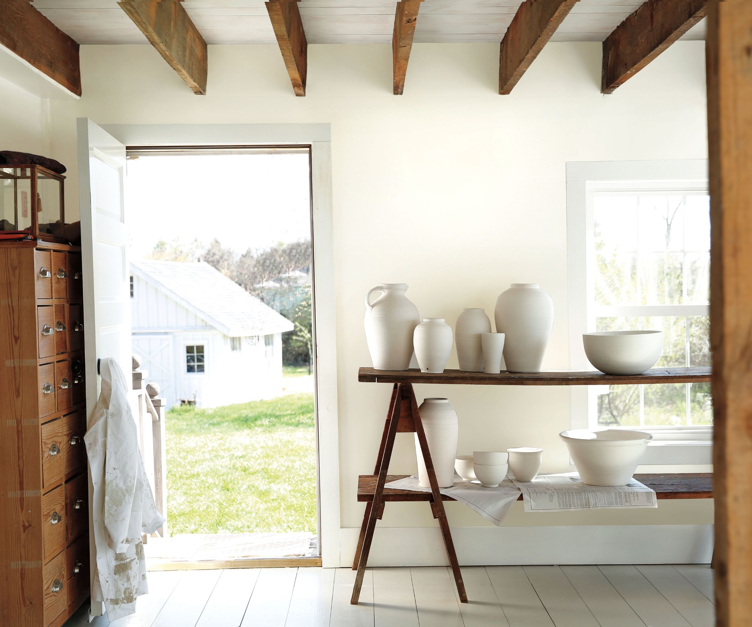 Entryway with beamed ceiling, wooden dresser, wooden bench holding ceramics, and white walls