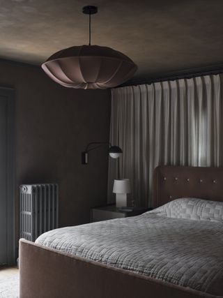 Brown bedroom with brown painted walls and a soft brown bed frame. The back wall is covered in a linen fabric