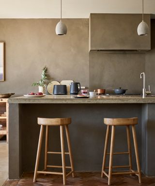 An industrial chic kitchen with brown chalk effect walls, grey concrete island, wooden bar stools and Herringbone flooring