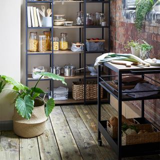 compact black kitchen trolley on castors in a kitchen with wooden floorboards, pot plants and a black and wooden display unit