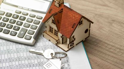 Photo of a calculator, a set of keys and a model house on top of financial papers