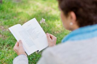 A woman reading a poetry anthology in a park while holding a flower.