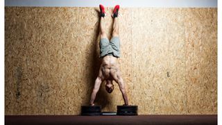Man performing a hanstand push up against a wall with hands on weights