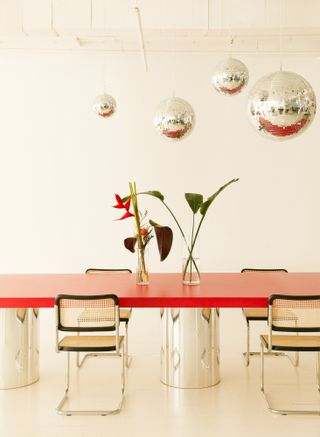 A large dining table with polished metal base and red lacquered tabletop, plus disco balls overhead