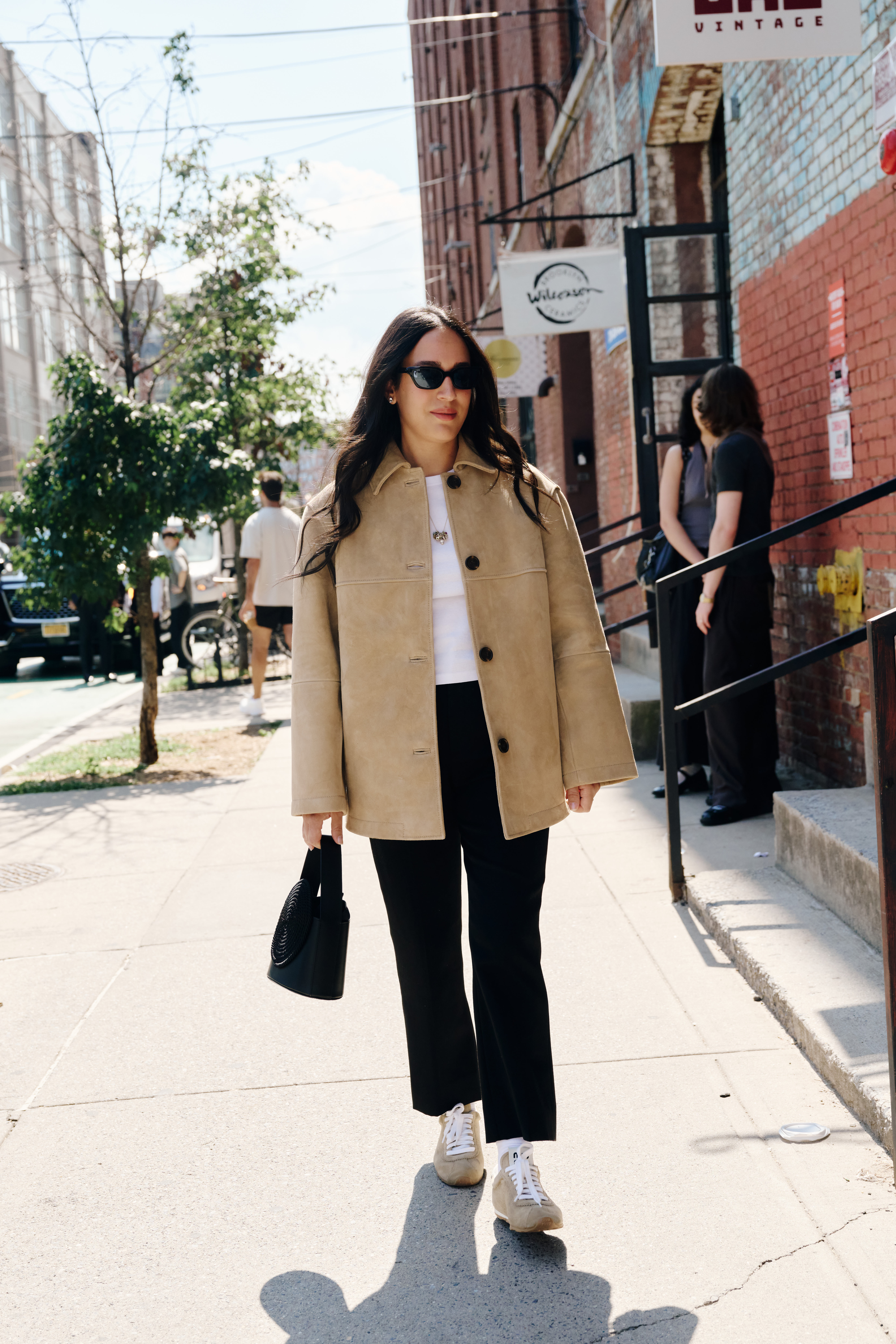 Nicole wears a suede jacket, white tee, black pants, and suede sneakers.