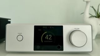 Rotel's DX-5 integrated amp in silver on a light gray table, with the amp's remote visible