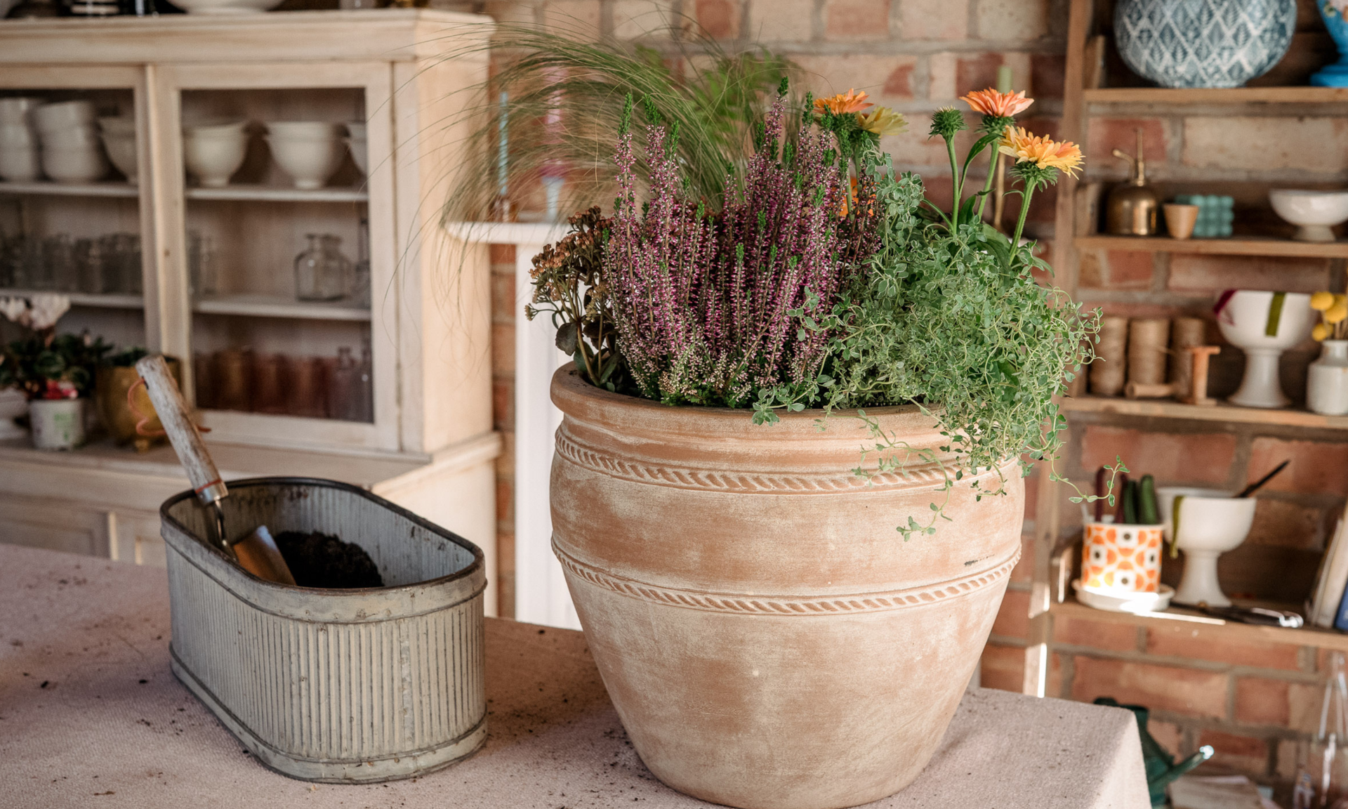 Workbench with large terracotta pot full of fall plants and zinc planter filled with soil