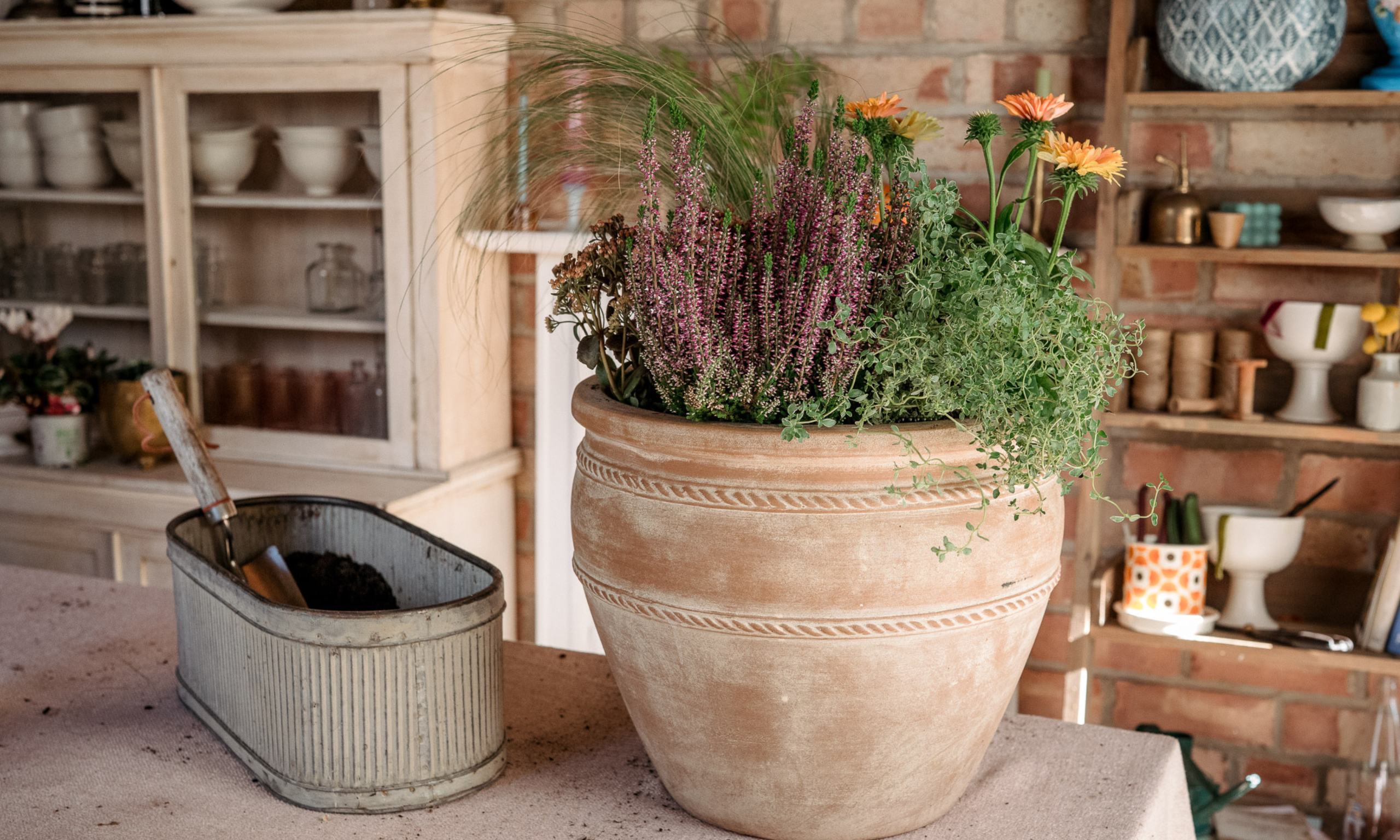 Workbench with large terracotta pot full of fall plants and zinc planter filled with soil