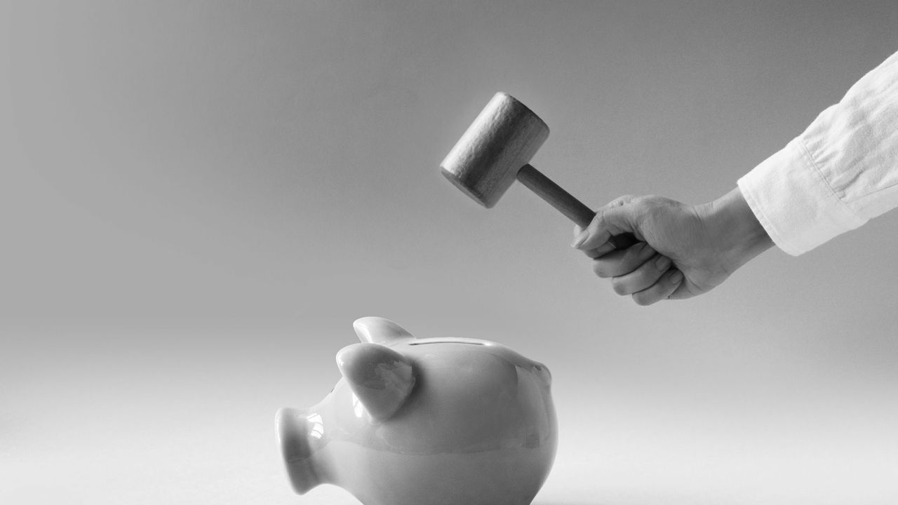 women hand using hammer trying to break a pink colour piggy bank on blue background