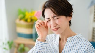 Woman indoors with hay fever rubbing sore eyes
