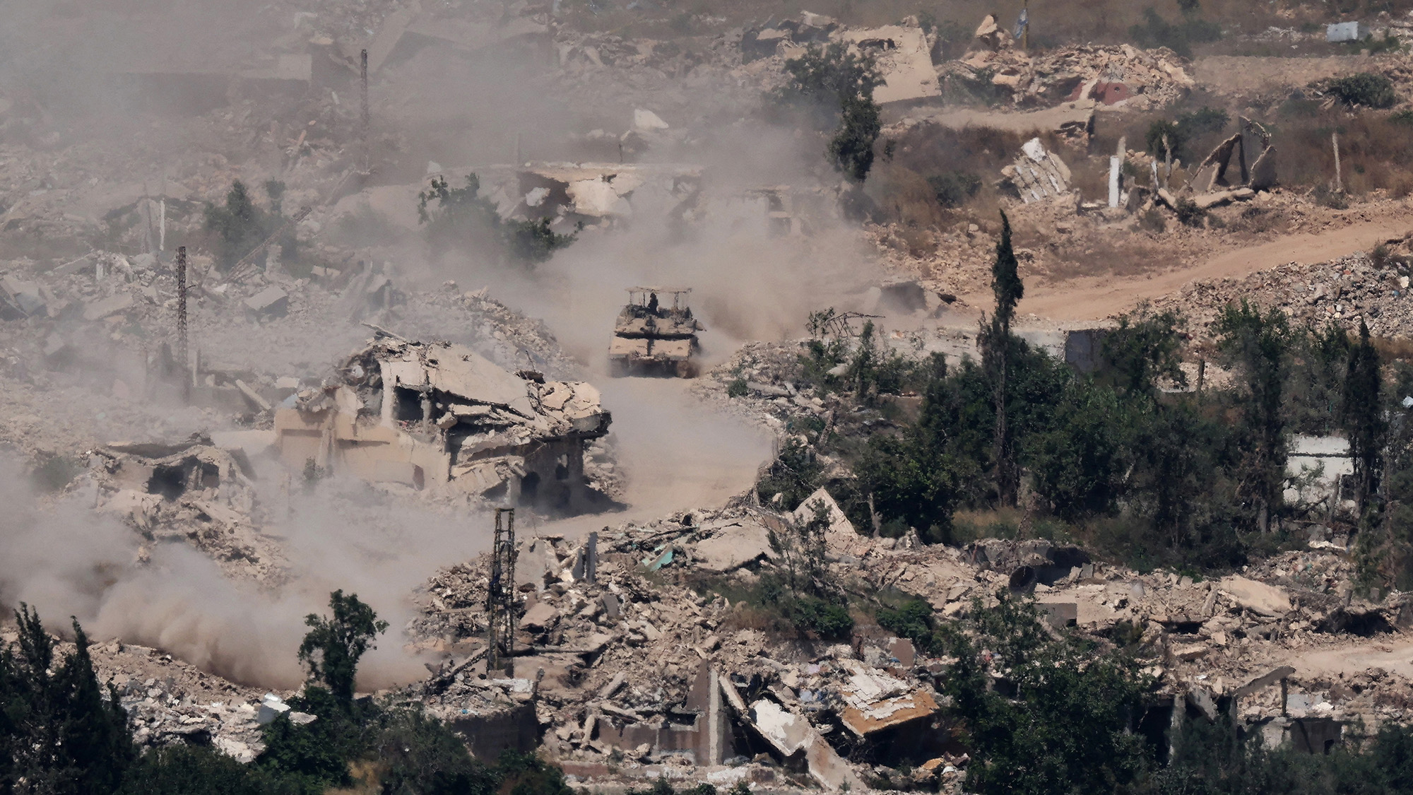 Israeli Merkava tanks drive along a road past destroyed buildings in southern Lebanon