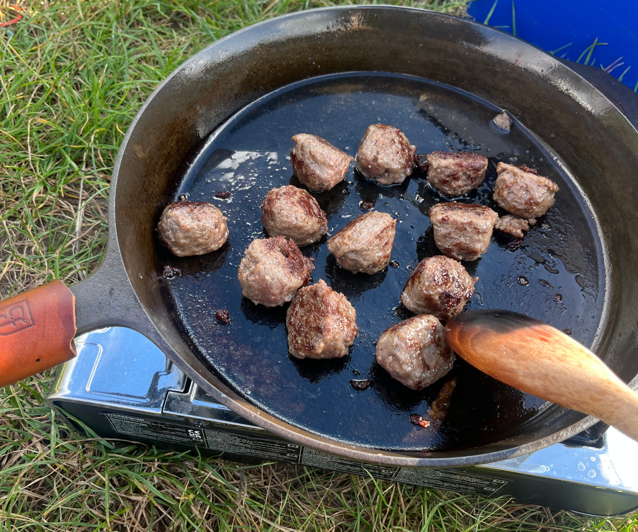 Field Company Skillet on an outside gas burner on grass, frying meatballs.