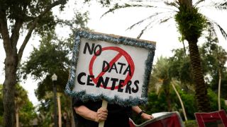 A person holding up a sign reading 'No data centers' in front of trees