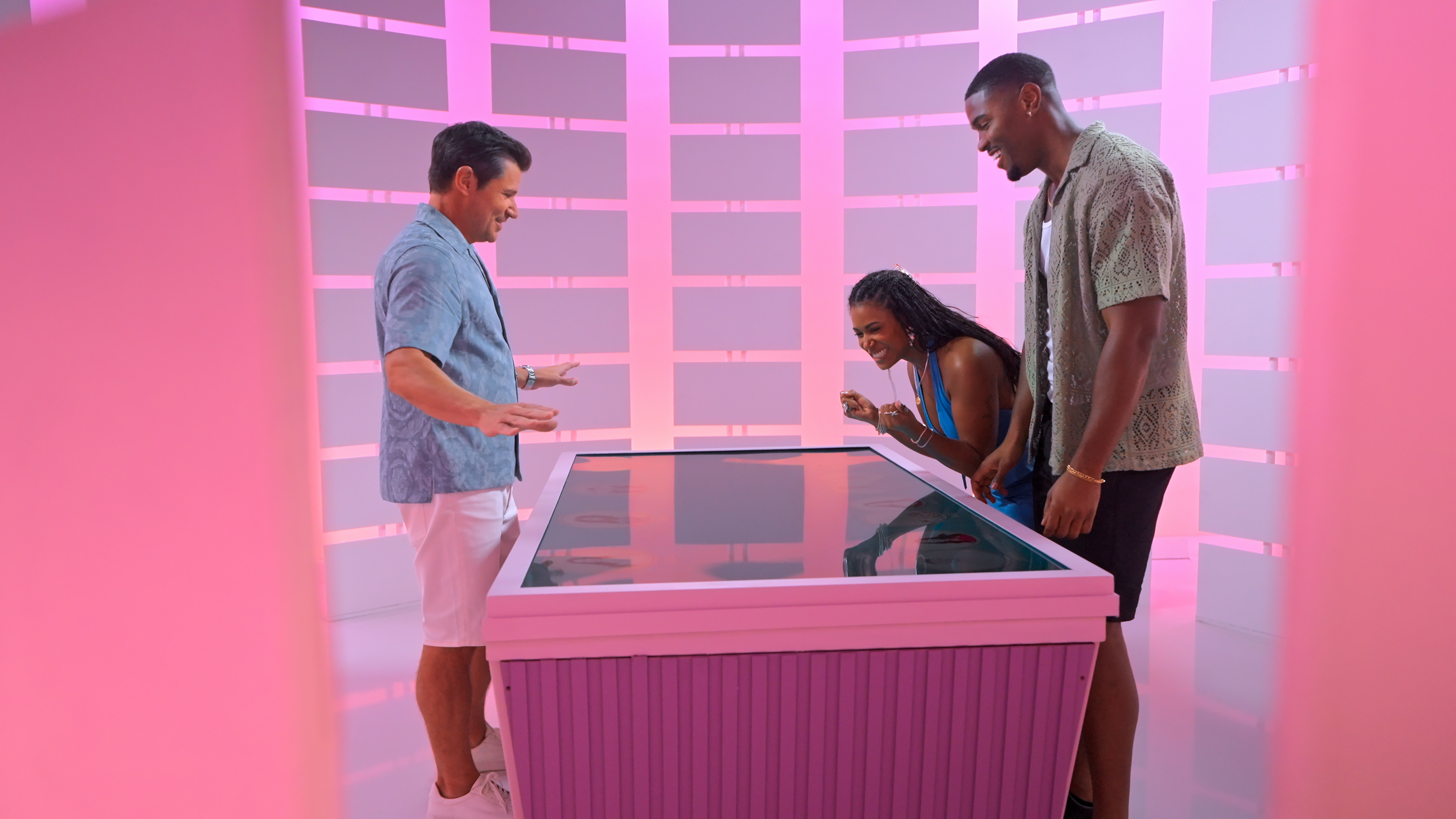 Nick Lachey, Marissa and Demari look down at a touchscreen podium in a neon-lit chamber called the Boardroom, in Netflix's 'Perfect Match' season 4.