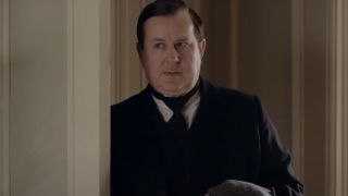 Jeremy Swift stands while listening in on a conversation in Downton Abbey.