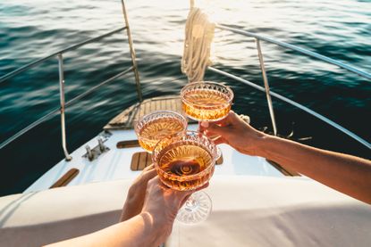 A close-up shot of friends clinking sparkling wine glasses at sunset on a yacht 