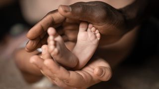 close-up of an adult&#039;s hands cupping a baby&#039;s feet 