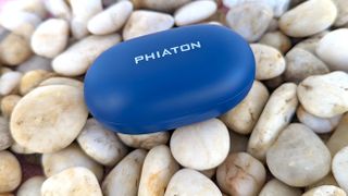 The Phiaton BonoBuds charging case placed atop a group of pebbles