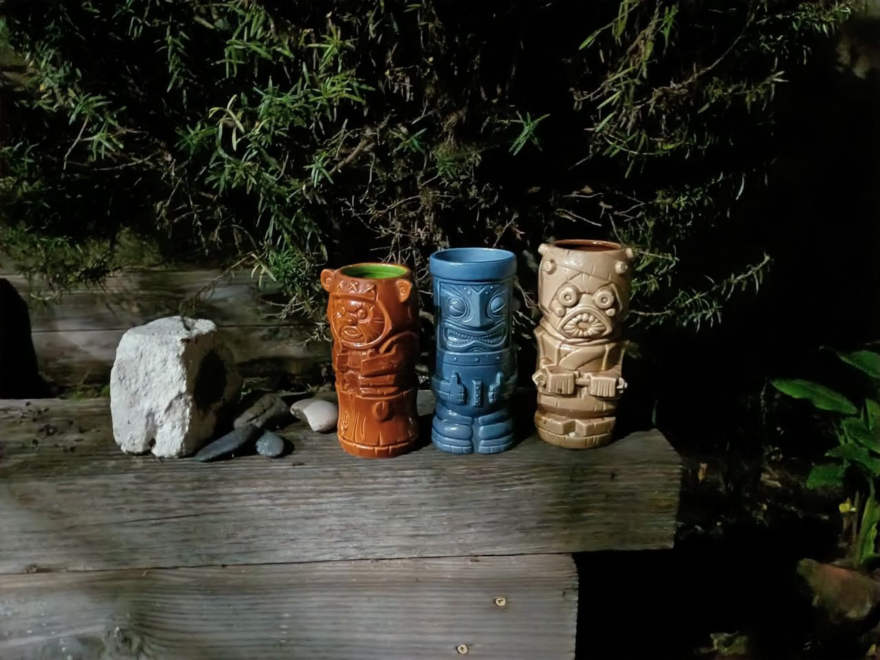four ceramic ornaments on a wooden shelf in a garden in artificial light in the nighttime