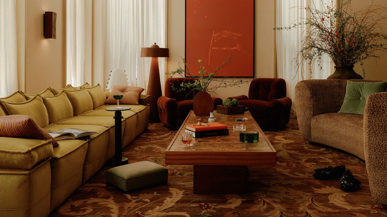 a 70s inspired living room with a yellow couch and oxblood armchairs with a patterned carpet