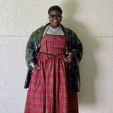 Lydia Okello wearing a plaid dress with a leather jacket in front of a plain wall