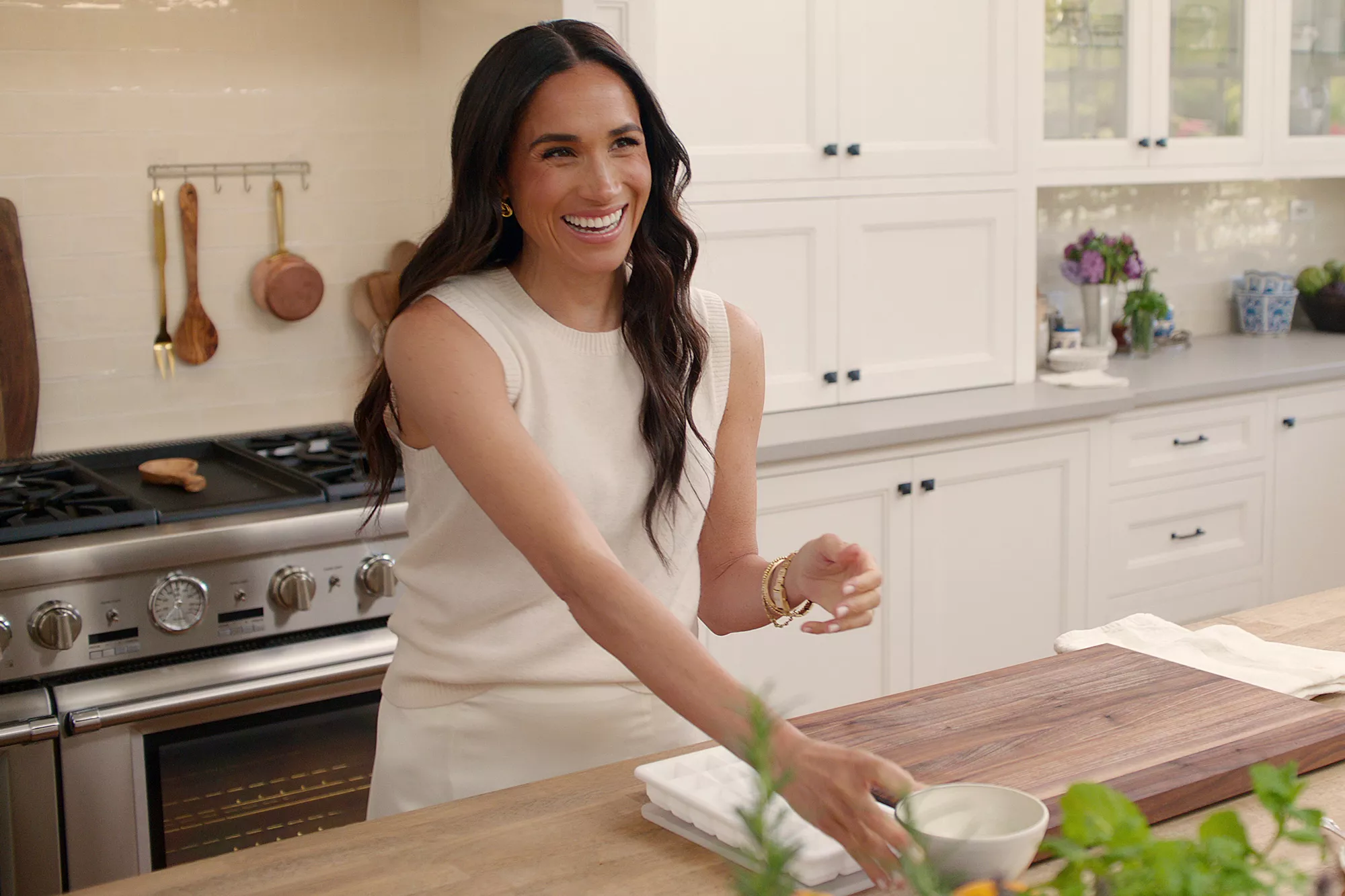Meghan Markle cooking in a white kitchen and smiling