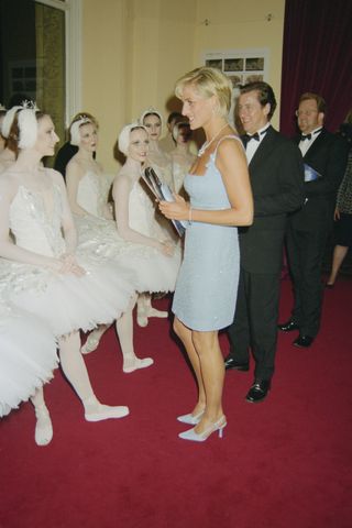 Princess Diana wearing a blue dress talking to ballet dancers wearing white tutus