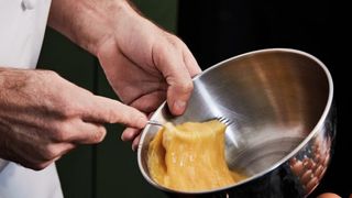 Hands using fork to beat eggs in a stainless steel mixing bowl