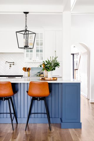 Blue painted island with leather barstools in kitchen with white walls