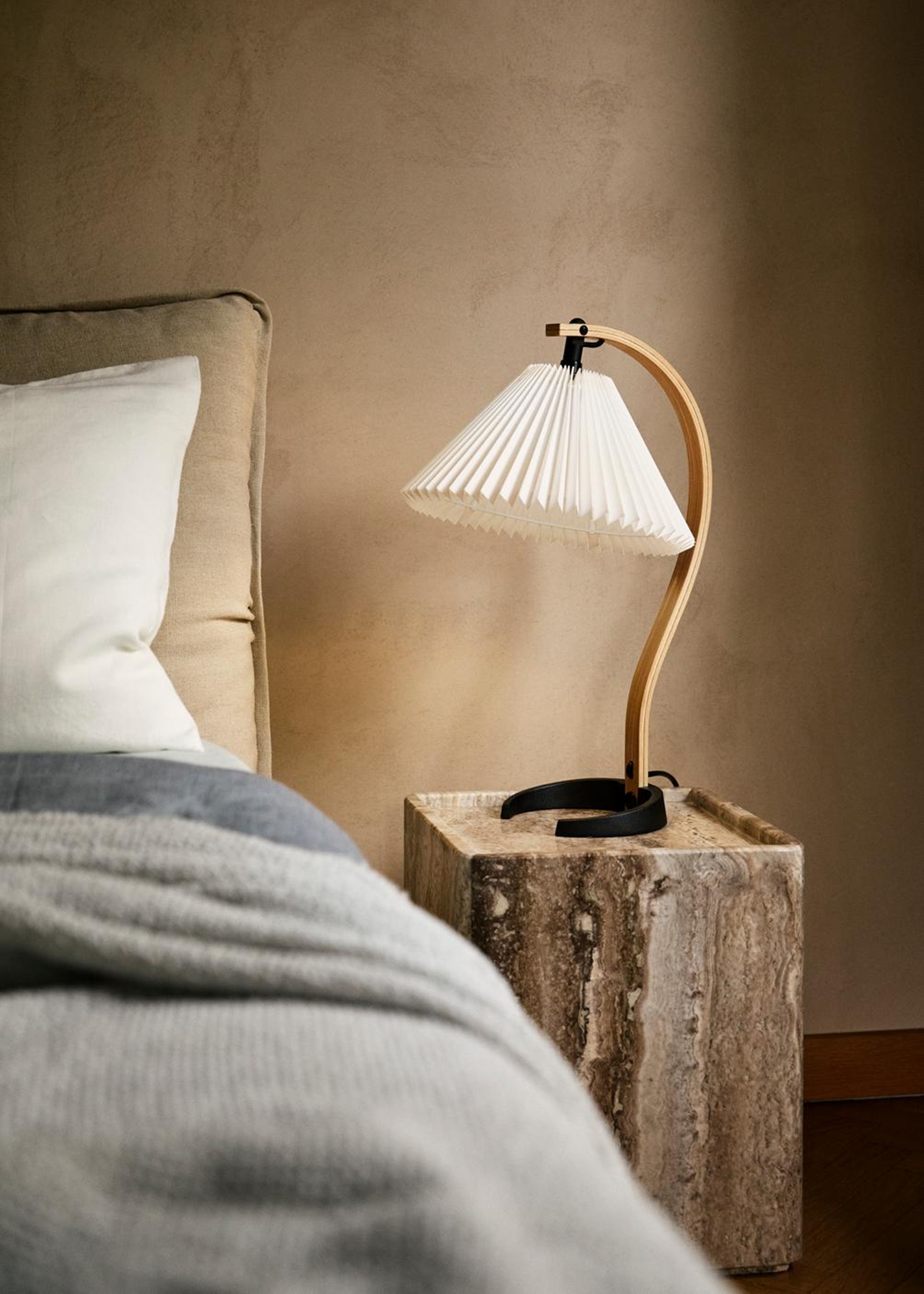 a gubi table lamp on a stone nightstand next to a bed