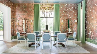 dining room with copper wallpaper, green curtains, gold chandelier, wooden dining table and blue and white dining chairs 